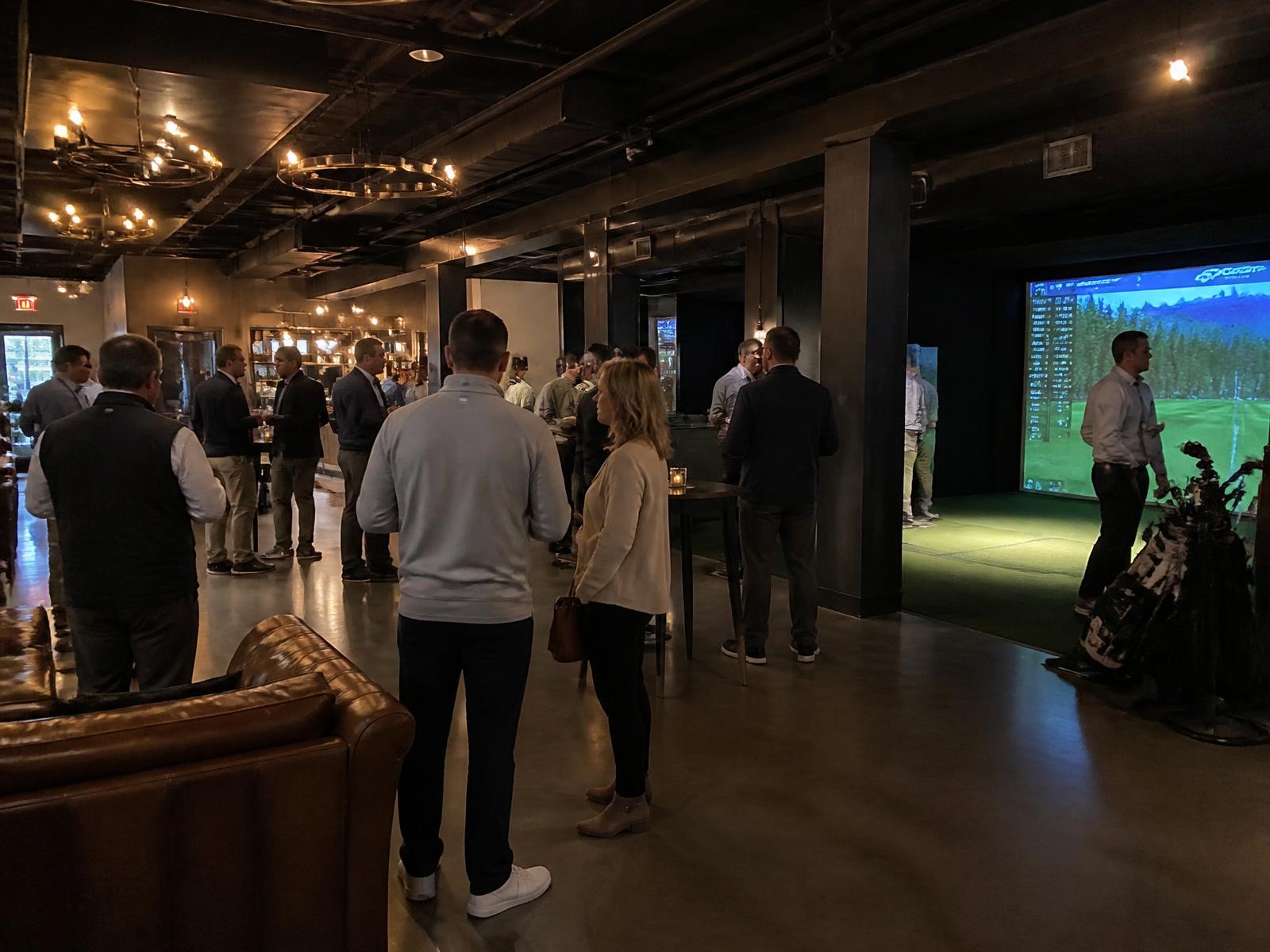 Private group event at Tee and Tap with guests mingling beside a lit simulator bay