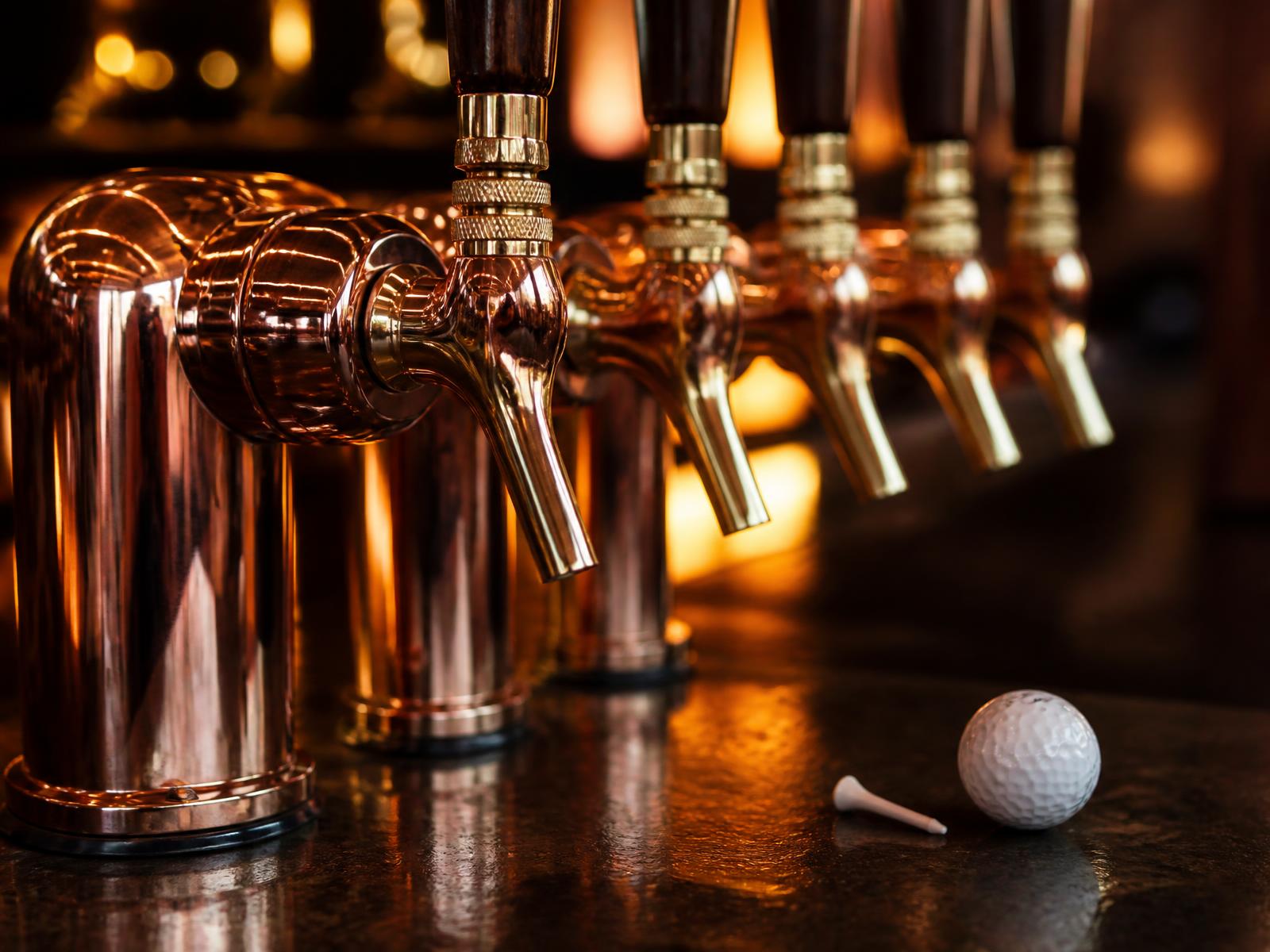 Row of polished copper tap handles with a golf ball and tee resting on the bar top